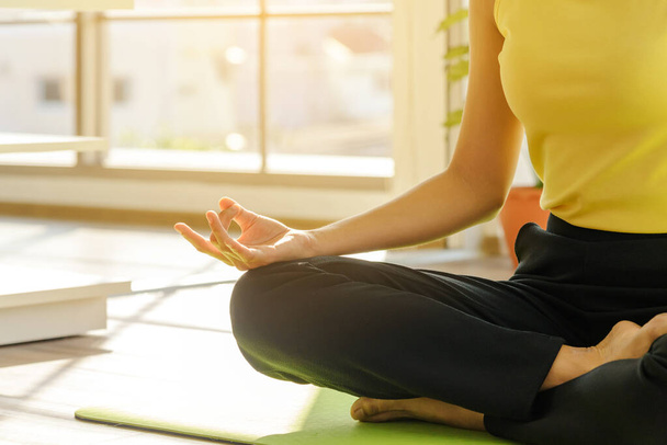 Vicino alla mano femminile mentre la donna asiatica pratica lezioni di yoga, respirazione, meditazione in soggiorno a casa. - Foto, immagini