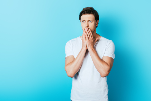 Sad man with hands near mouth looking away on blue background - Foto, afbeelding
