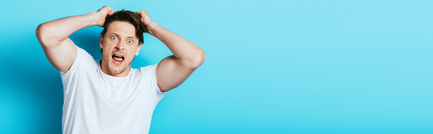 Panoramic orientation of crazy man in white t-shirt looking at camera on blue background - Photo, Image