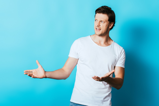 Aggressive man pointing with hands while looking away on blue background - Valokuva, kuva