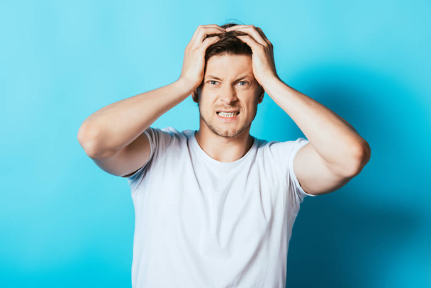 Young angry man in white t-shirt looking at camera on blue background - Photo, Image