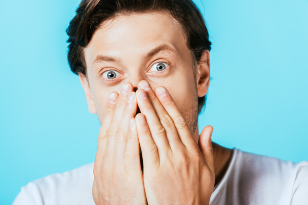 Shocked man looking at camera and covering mouth isolated on blue  - Photo, Image