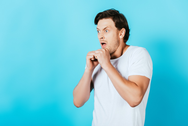 Crazy man in white t-shirt with hands in fists looking away on blue background - Fotografie, Obrázek