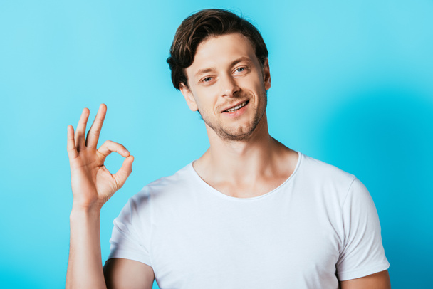 Man in white t-shirt showing okay gesture on blue background - Fotografie, Obrázek