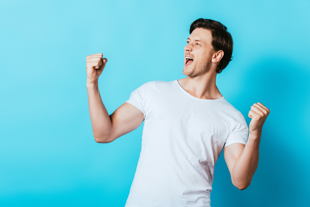 Young man in white t-shirt showing yes gesture on blue background - Fotoğraf, Görsel