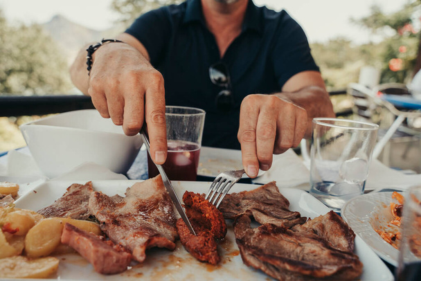 50-летний взрослый мужчина в очках и с белыми волосами, стригущий мясо в ресторане. - Фото, изображение