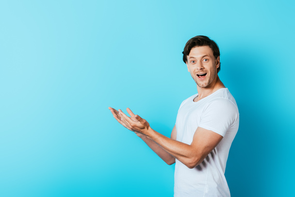 Young man in white t-shirt pointing with hands on blue background - Valokuva, kuva