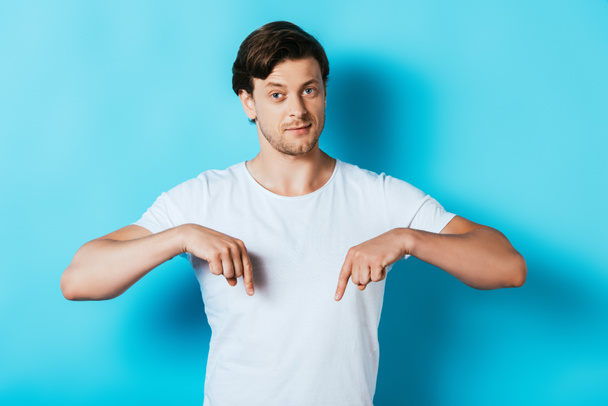 Uomo sicuro di sé in t-shirt bianca che punta con le dita su sfondo blu - Foto, immagini