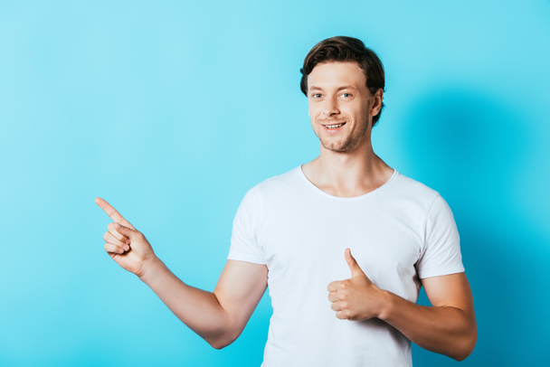 Young man in white t-shirt pointing with finger and showing like gesture on blue background - Foto, imagen