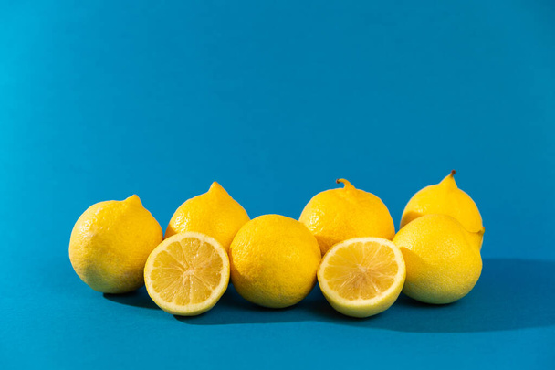 group of six yellow lemons (fruit) and two halves. blue background. studio photo. - Photo, image