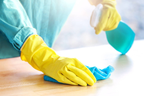 Vrouw met gele handschoenen die de tafel schoonmaakt met spray desinfectiemiddel in een restaurant of keuken. - Foto, afbeelding