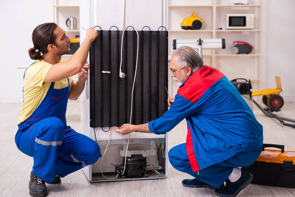 Dois empreiteiros reparando geladeira na oficina
 - Foto, Imagem