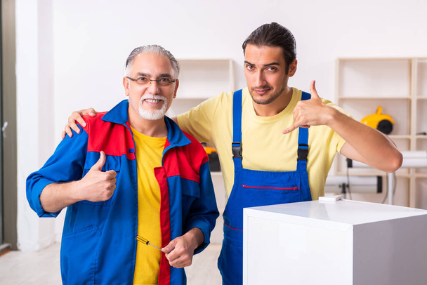 Twee aannemers repareren koelkast in werkplaats - Foto, afbeelding