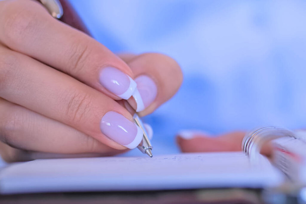 Frau hält Stift in der Hand und schreibt Aufgabenliste in Notizbuch - Foto, Bild