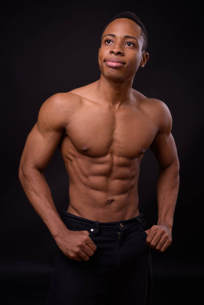Studioaufnahme eines jungen, gut aussehenden, muskulösen afrikanischen Mannes ohne Hemd vor schwarzem Hintergrund - Foto, Bild