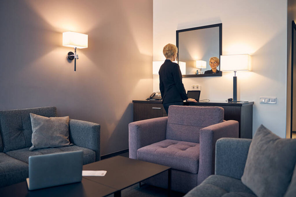Όμορφη γυναίκα κοιτάζει στον καθρέφτη στο δωμάτιο του ξενοδοχείου - Φωτογραφία, εικόνα
