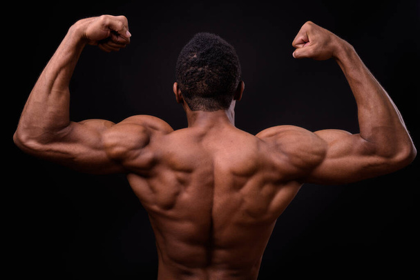 Studio shot of young handsome muscular African man shirtless against black background - Foto, imagen