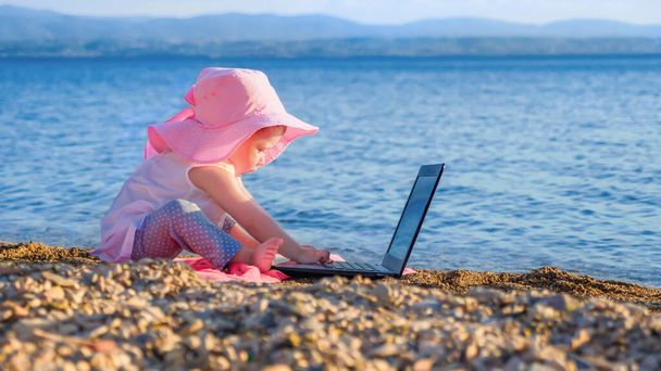 Little girl with notebook on seashore. Holiday on greek seashore background concept. Two year old business kid on seaside. Childhood concept. Happiness background. Modern children and gadgets - Photo, Image