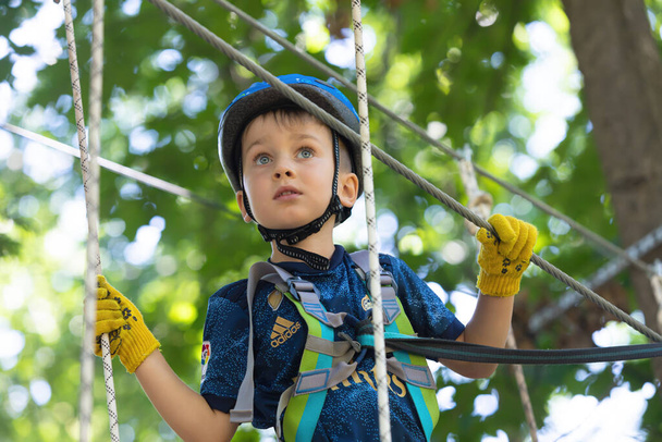 UZHHOROD, UKRAINE - Jul 23, 2020: Extreme sport in adventure park. Young boy passing the cable route high among trees - Photo, Image