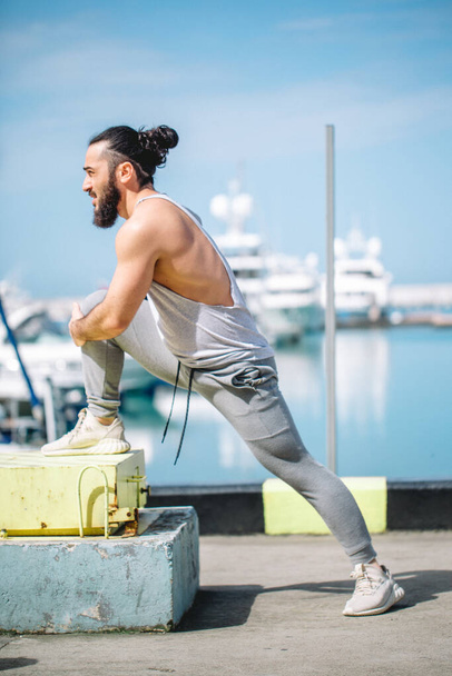 Sportsman with trendy hairstyle stretching body while standing at the sea pier - Fotoğraf, Görsel