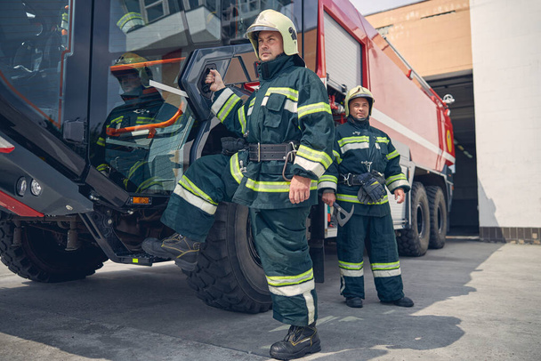 Man putting his foot on step of big red fire truck - Фото, изображение
