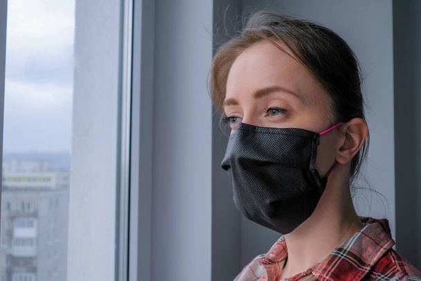 Töprengő nő orvosi maszkot visel, és kinézett az ablakon - közelről - Fotó, kép