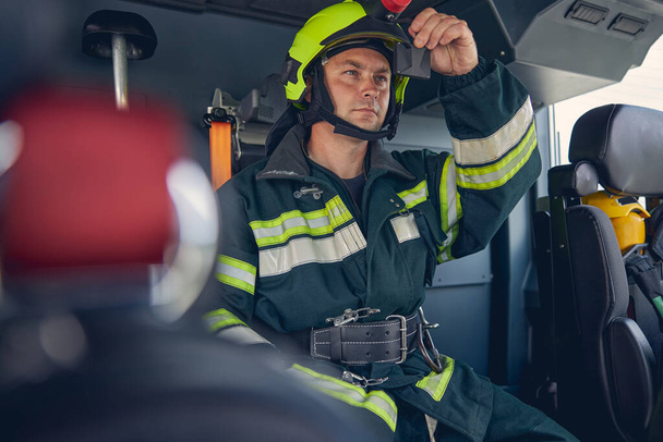 Male wearing green protective uniform and helmet siting in the machine - Fotografie, Obrázek