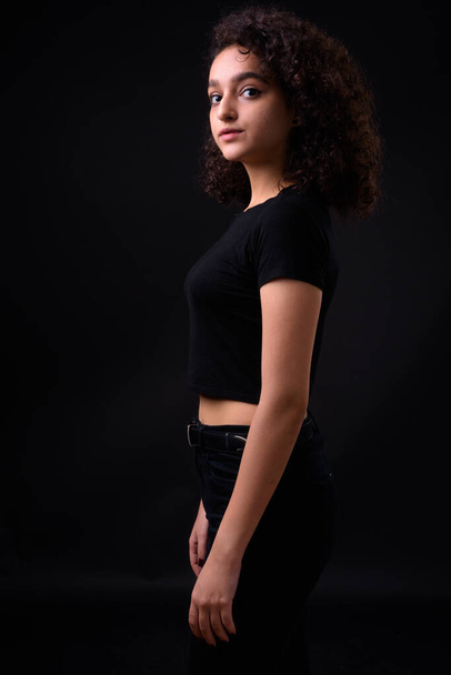 Studio shot of young beautiful Iranian teenage girl with curly hair against black background - Foto, afbeelding