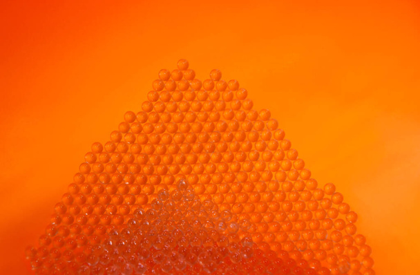 Kis üveg szilárd golyók narancs háttér stock képek. Egy halom kristálytiszta gyöngyös kép. Fényes narancs háttér textúra képek. Kis szilárd boroszilikát üveggolyók képek - Fotó, kép