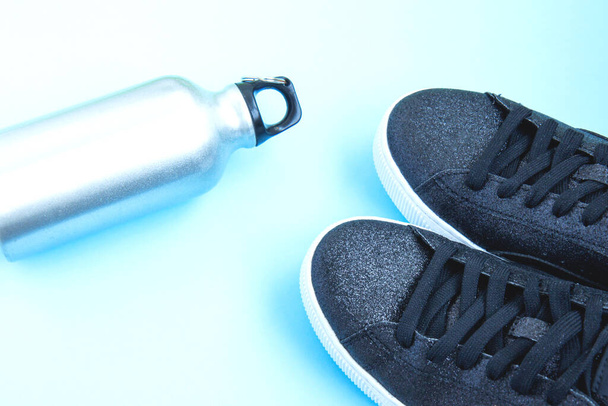 Sapatilhas pretas e garrafa de ferro de água no fundo azul
 - Foto, Imagem
