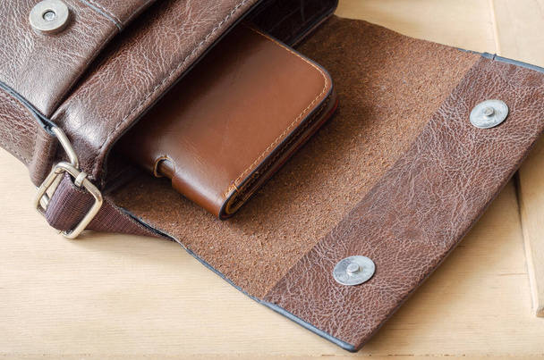 ブラウンレザー財布内部小さなショルダーバッグ。木製の背景にオープンバッグと茶色の革財布。角度でトップビュー。選択的焦点. - 写真・画像