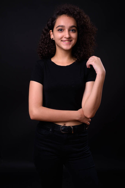 Studio shot of young beautiful Iranian teenage girl with curly hair against black background - Photo, Image