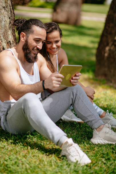 Man and woman relaxing with digital tablet in park after sports training - Valokuva, kuva