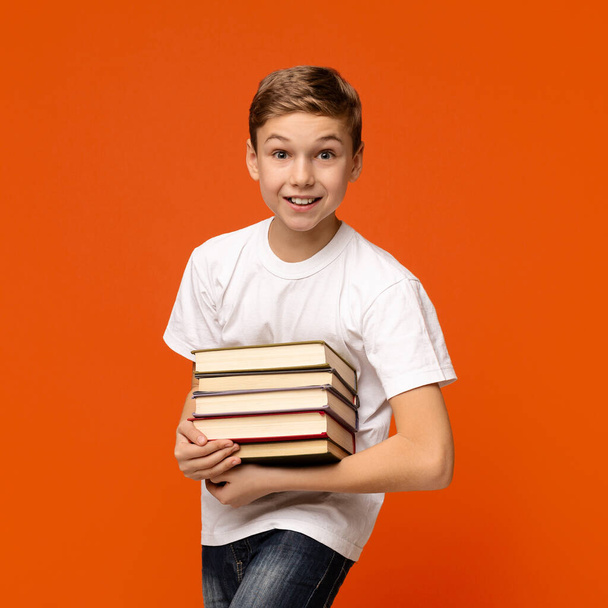 Teen boy smiling with heap of books in hands - 写真・画像