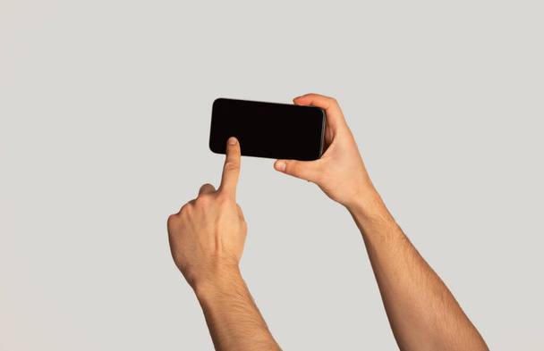 Nierozpoznawalny tysiącletni mężczyzna dotykający ekranu telefonu komórkowego na jasnym tle, przestrzeń do projektowania aplikacji mobilnych - Zdjęcie, obraz