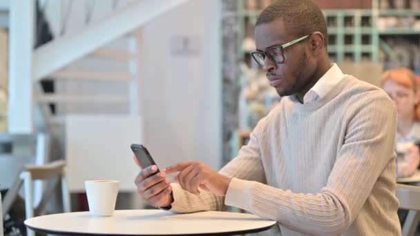 Ελκυστικός Αφρικανός που χρησιμοποιεί Smartphone στο Cafe  - Πλάνα, βίντεο
