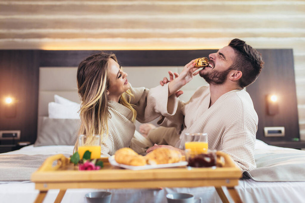 Smiling couple having breakfast in bed in hotel room - Photo, image