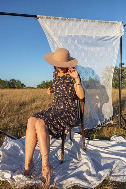 Mujer joven bastante fresco sentado en la silla al aire libre en el campo y usar en vestido en el fondo un estante con cortinas blancas. Concepto de vacaciones de verano en el pueblo y estilo en vivo - Foto, Imagen