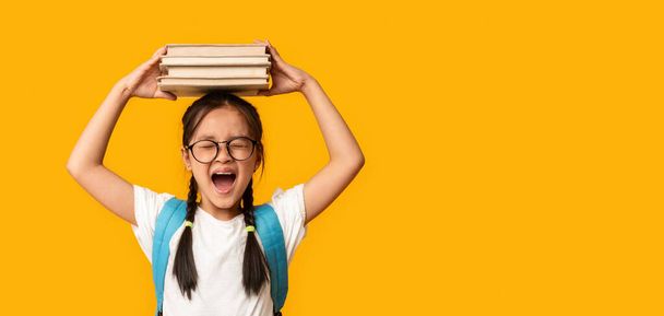 Érzelmi ázsiai iskolás sikoltozó pózol könyvek felett sárga háttér - Fotó, kép