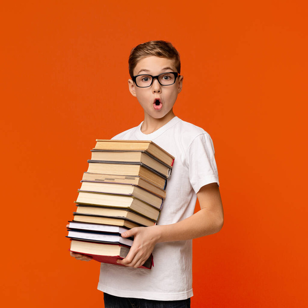 Geschokt schooljongen in bril houden stapel boeken - Foto, afbeelding