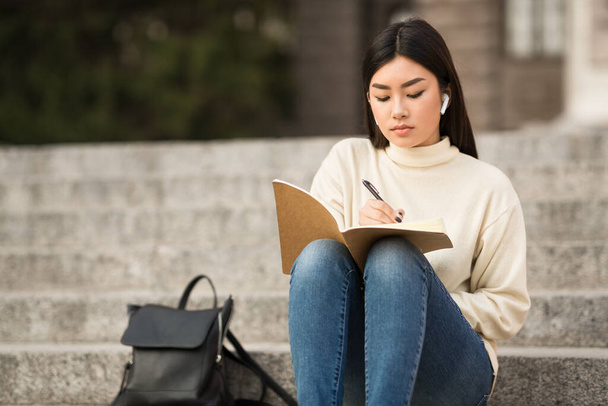 Schrijvend meisje in dagboek, zittend op de grijze treden - Foto, afbeelding