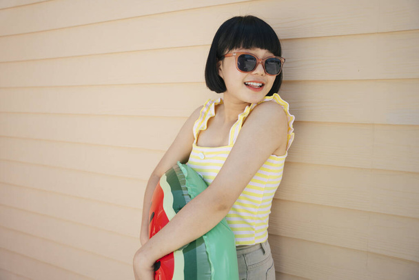 Bob corte de pelo hermosa mujer asiática joven con camiseta de tanque amarillo y gafas de sol posando con salvavidas o tubo de natación. - Foto, imagen