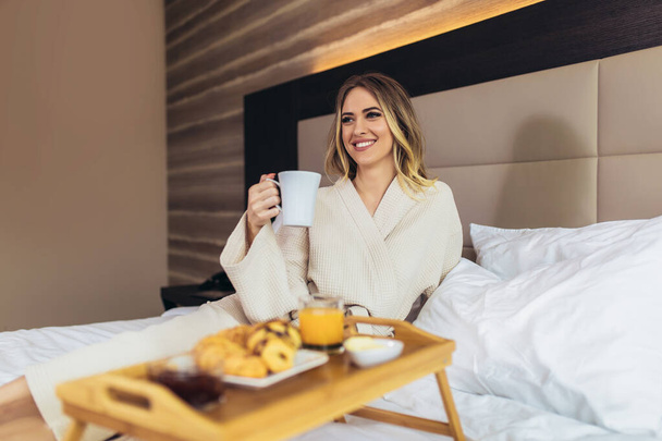 Relaxovaná žena se snídaní v posteli, doma nebo v hotelovém pokoji - Fotografie, Obrázek