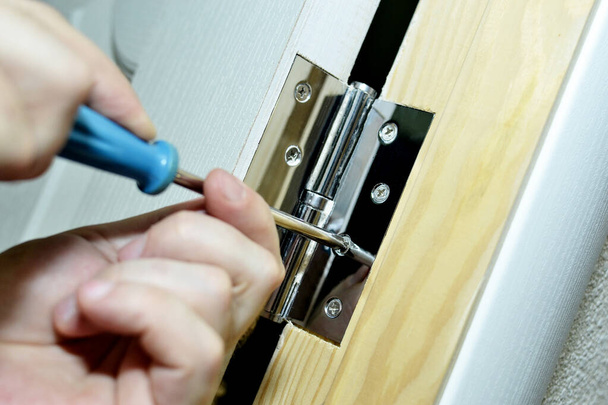 trabajador haciendo renovaciones en el hogar instala bisagras de la puerta con un destornillador - Foto, Imagen