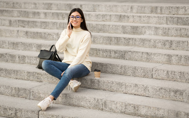 Γυναίκα φοιτήτρια που χρησιμοποιεί το τηλέφωνο, κάθεται στις σκάλες - Φωτογραφία, εικόνα