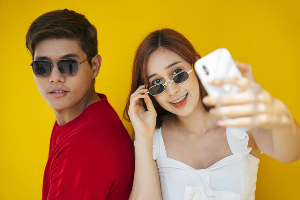Close up jovem asiático tailandês casal vestindo óculos tomando selfie com smartphone sobre fundo laranja
. - Foto, Imagem