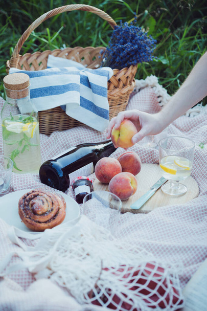 Summer - lemonade with lemon and mint with wine, peaches, cinnamon rolls, candles and a bouquet and a baske - Фото, изображение