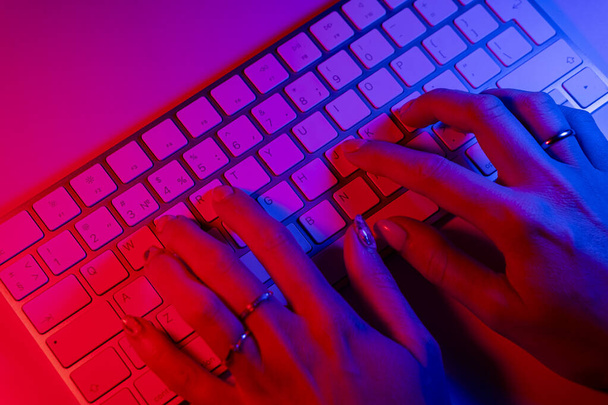 Una mujer que trabaja en un ordenador portátil desde casa. Gente de negocios estilo de vida. Mujer escribiendo en el ordenador portátil en tonos azules y rosados. Mujer mensaje de escritura a mano en el teclado del ordenador. - Foto, Imagen
