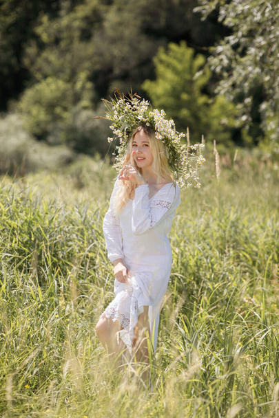 Νεαρή λευκή γυναίκα με ξανθά μαλλιά ντυμένη με λευκό φόρεμα το καλοκαίρι σε χωράφι - Φωτογραφία, εικόνα