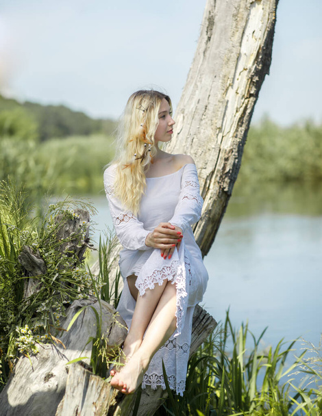 Jeune femme blanche aux longs cheveux blonds près d'une rivière dans une forêt - Photo, image